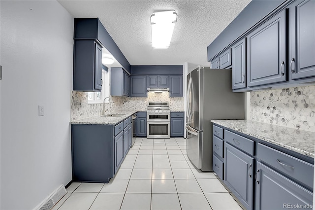 kitchen featuring sink, a textured ceiling, light tile patterned floors, appliances with stainless steel finishes, and light stone countertops