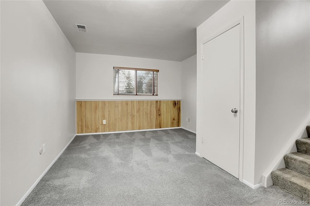 carpeted empty room with stairs, wainscoting, visible vents, and wooden walls