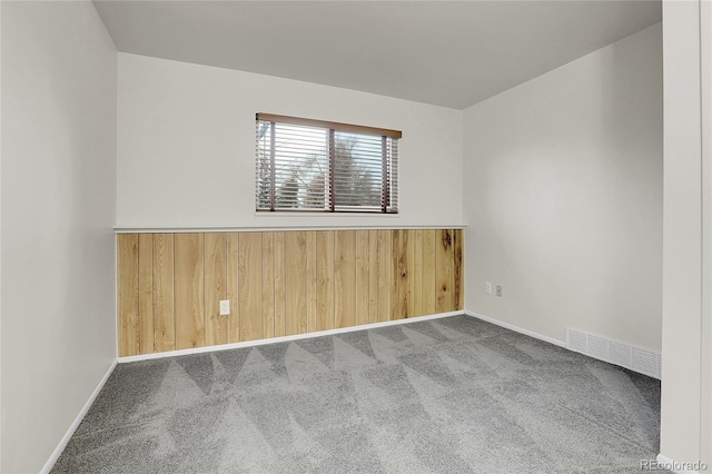 carpeted empty room with wood walls, baseboards, and visible vents