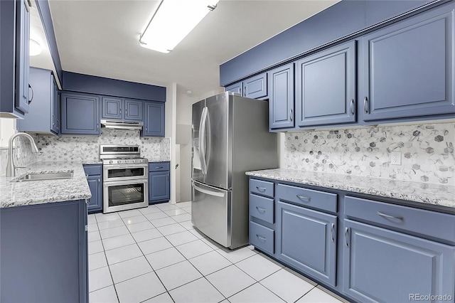 kitchen with light tile patterned flooring, under cabinet range hood, stainless steel appliances, a sink, and blue cabinetry