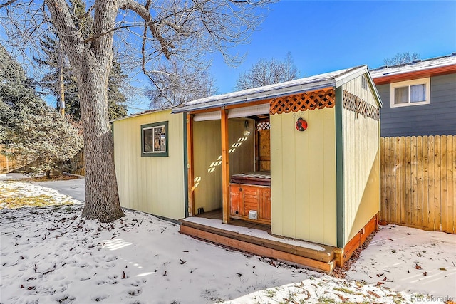 snow covered structure featuring fence and an outbuilding