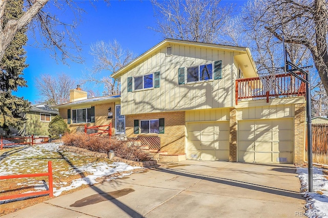 split level home with concrete driveway, a chimney, an attached garage, fence, and brick siding