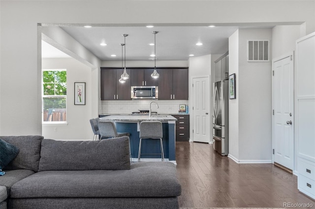 kitchen featuring stainless steel appliances, open floor plan, dark brown cabinetry, dark wood-style floors, and a kitchen breakfast bar
