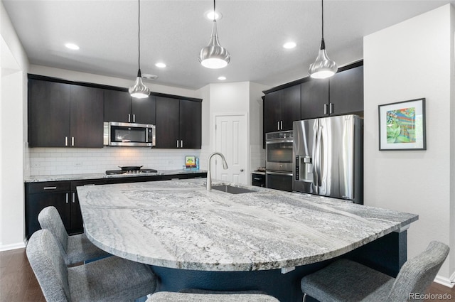 kitchen with appliances with stainless steel finishes, a sink, a kitchen bar, dark wood-style floors, and recessed lighting