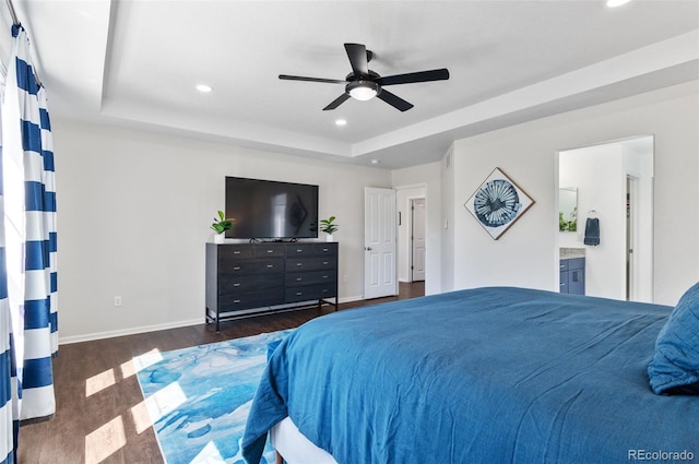 bedroom with dark wood-style flooring, a tray ceiling, recessed lighting, baseboards, and ensuite bathroom
