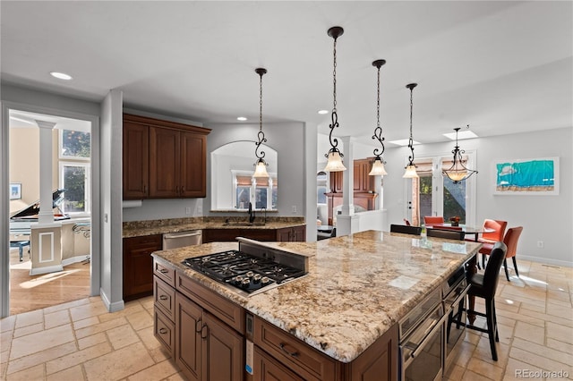 kitchen featuring sink, appliances with stainless steel finishes, hanging light fixtures, light stone counters, and a kitchen island