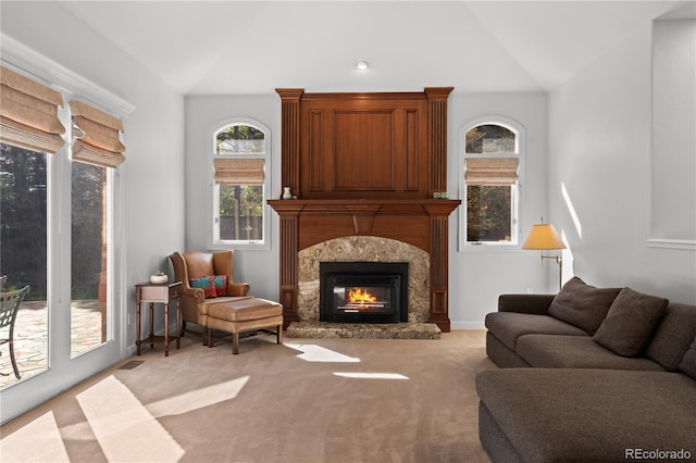 carpeted living room featuring a high end fireplace and vaulted ceiling