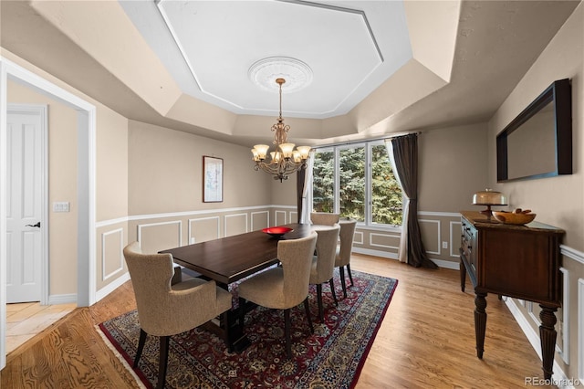 dining space featuring a notable chandelier, a tray ceiling, and light wood-type flooring