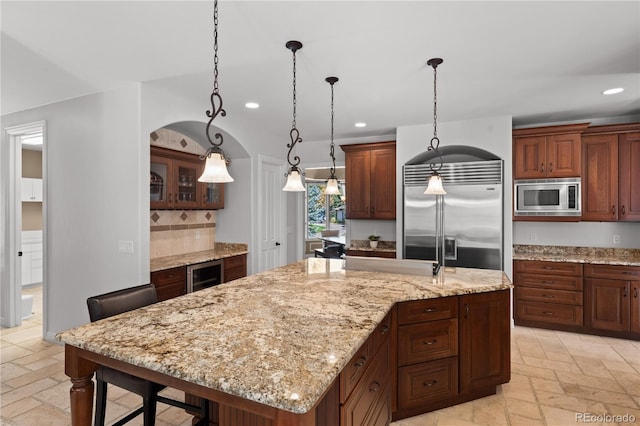 kitchen with pendant lighting, beverage cooler, backsplash, a kitchen island with sink, and built in appliances