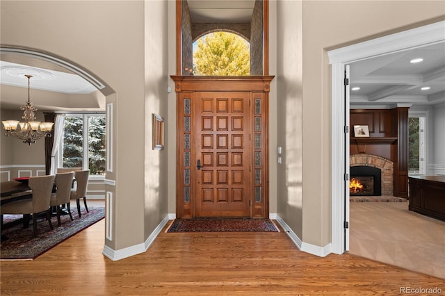 entrance foyer with coffered ceiling, a fireplace, light hardwood / wood-style flooring, and a chandelier