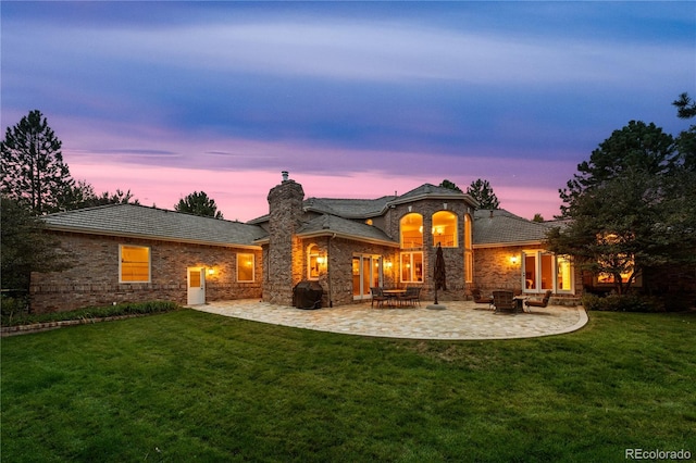 back house at dusk with a fire pit, a lawn, and a patio area