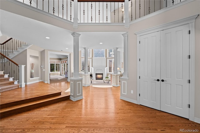 foyer entrance with decorative columns, a towering ceiling, and light wood-type flooring