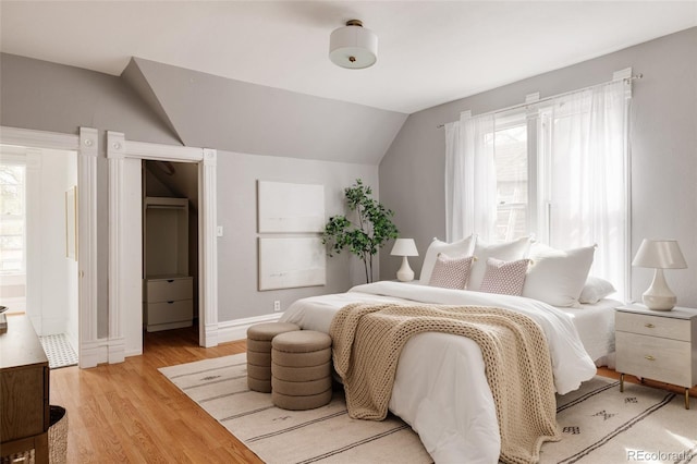 bedroom featuring baseboards, light wood-type flooring, and lofted ceiling