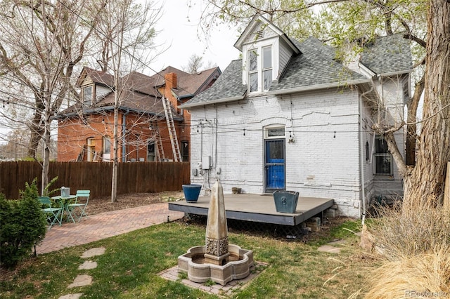 rear view of house with roof with shingles, a wooden deck, a patio area, brick siding, and fence