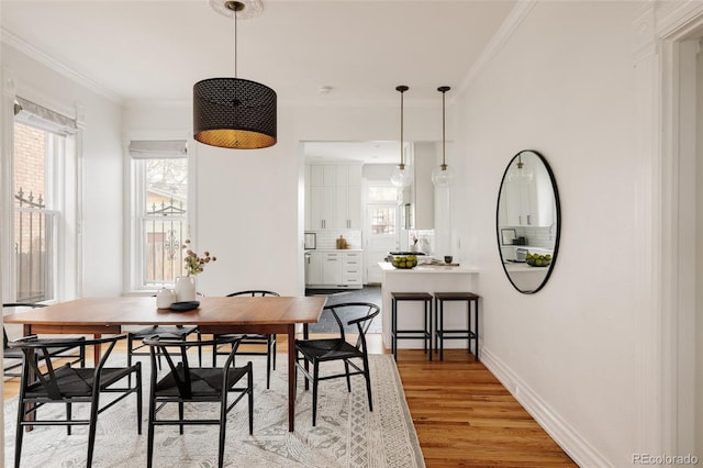 dining space featuring crown molding, light wood finished floors, and baseboards
