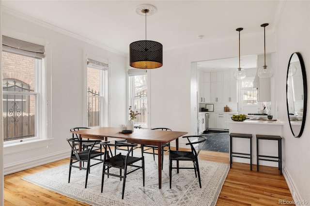 dining room with light wood-type flooring, ornamental molding, and baseboards