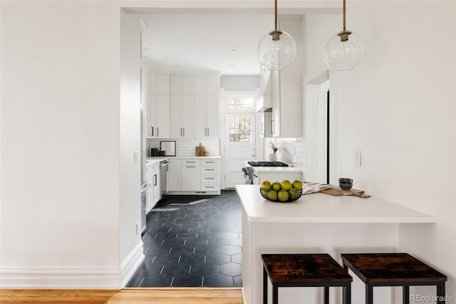 kitchen with dishwasher, a breakfast bar area, white cabinetry, backsplash, and gas stove