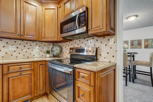 kitchen with decorative backsplash, light stone counters, stainless steel appliances, and a textured ceiling