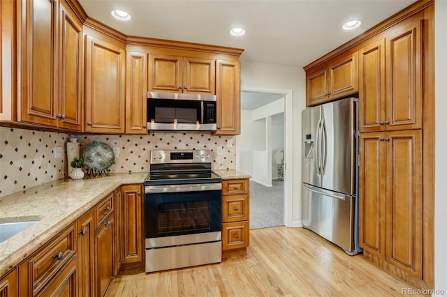 kitchen with light stone counters, decorative backsplash, stainless steel appliances, and light wood-type flooring