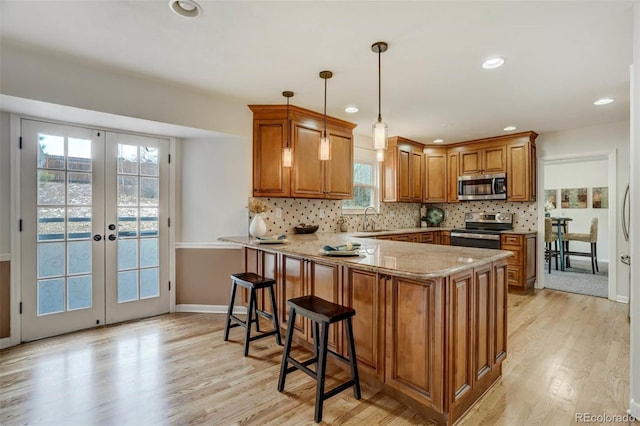 kitchen with kitchen peninsula, appliances with stainless steel finishes, light wood-type flooring, french doors, and hanging light fixtures