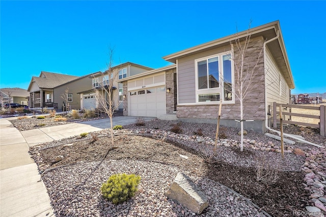 view of front of property featuring fence, a residential view, concrete driveway, a garage, and stone siding