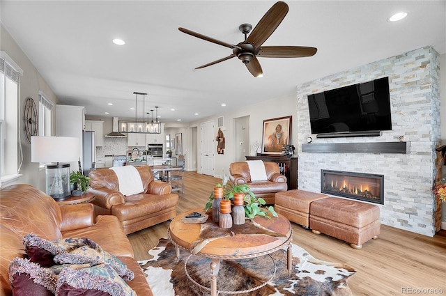 living room featuring ceiling fan, a stone fireplace, light wood-style flooring, and recessed lighting