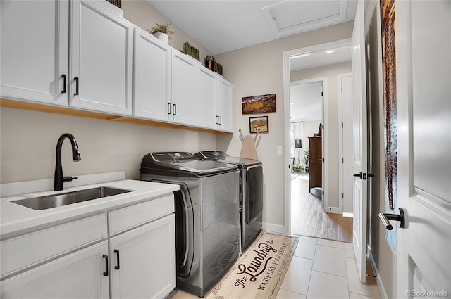 laundry area with attic access, light tile patterned floors, washer and dryer, cabinet space, and a sink