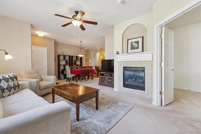 living room with a ceiling fan, a tile fireplace, light carpet, and baseboards