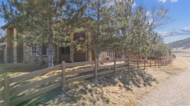 view of property hidden behind natural elements with a fenced front yard, stone siding, and a mountain view