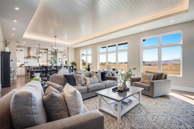 living room featuring a raised ceiling, light wood-style flooring, recessed lighting, an inviting chandelier, and baseboards