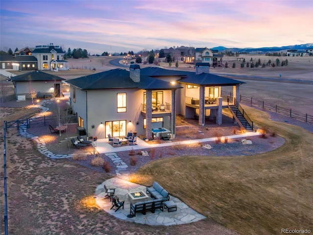 rear view of house with stucco siding, a patio, fence, an outdoor living space with a fire pit, and stairs