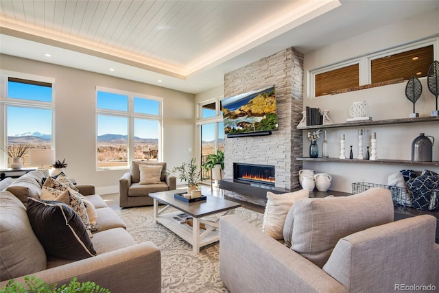 living room featuring a raised ceiling, recessed lighting, a stone fireplace, baseboards, and wood ceiling