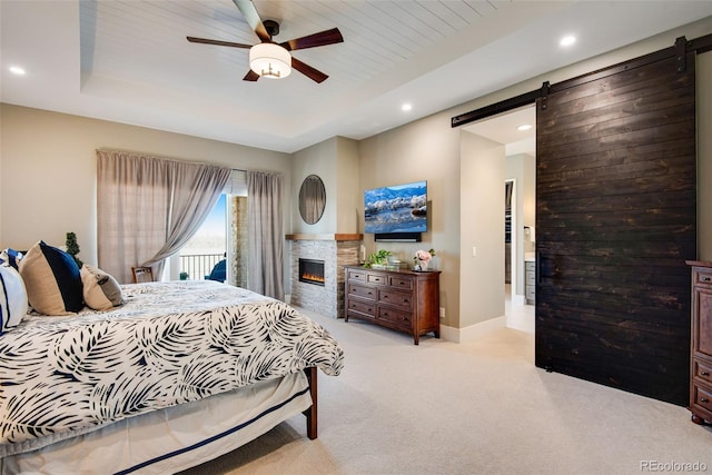 bedroom featuring a barn door, light carpet, recessed lighting, a glass covered fireplace, and a raised ceiling