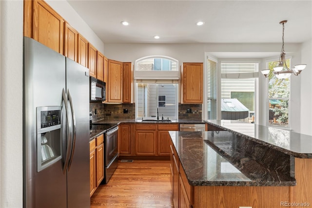 kitchen with sink, light hardwood / wood-style floors, appliances with stainless steel finishes, decorative light fixtures, and backsplash