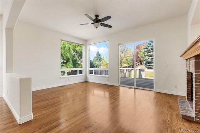 unfurnished living room with wood-type flooring, a brick fireplace, and ceiling fan