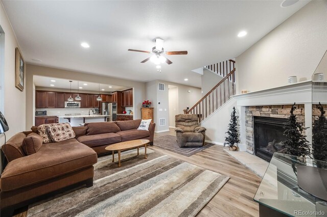 living room featuring a fireplace, sink, light wood-type flooring, and ceiling fan