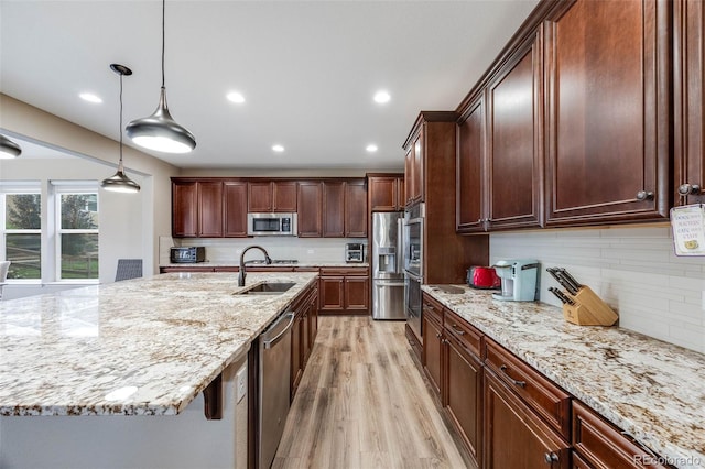 kitchen featuring appliances with stainless steel finishes, decorative light fixtures, an island with sink, sink, and light stone counters