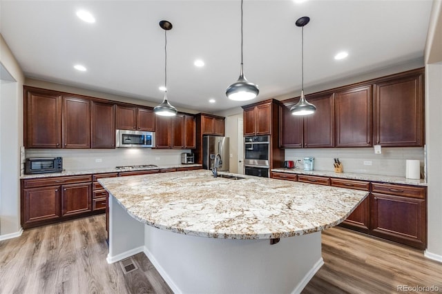 kitchen featuring pendant lighting, sink, appliances with stainless steel finishes, light hardwood / wood-style floors, and an island with sink