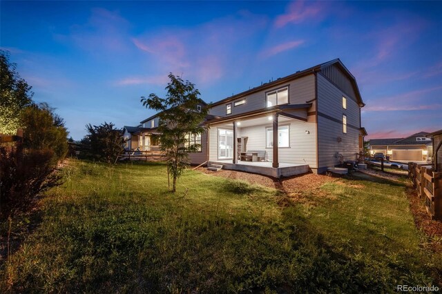 back house at dusk featuring a patio and a yard