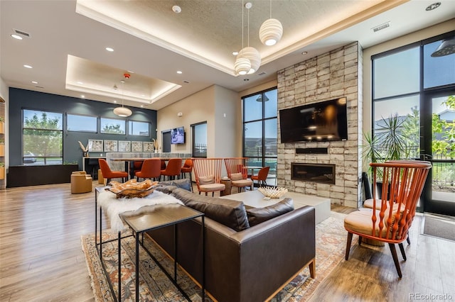 living room featuring a raised ceiling, a stone fireplace, and light hardwood / wood-style flooring