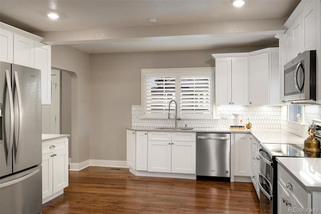 kitchen with arched walkways, a sink, decorative backsplash, stainless steel appliances, and white cabinets