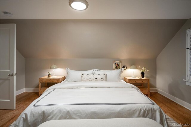 bedroom with baseboards, wood finished floors, and vaulted ceiling