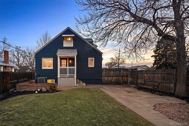 rear view of property featuring a yard, central AC, a fenced backyard, and a shingled roof