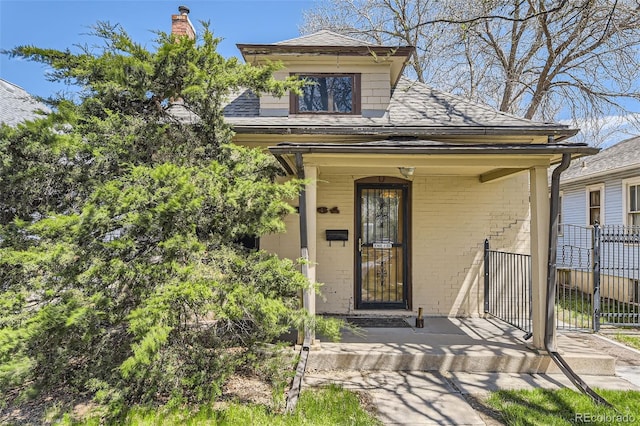 doorway to property with a porch, roof with shingles, fence, and brick siding