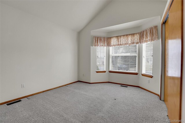 carpeted empty room with vaulted ceiling, visible vents, and baseboards