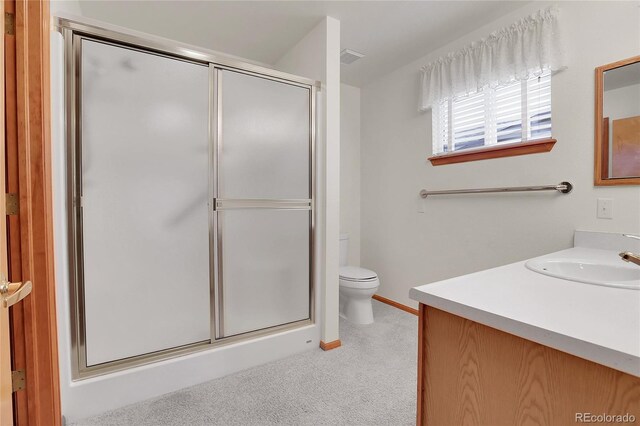 bathroom with toilet, vanity, a shower with shower door, and baseboards