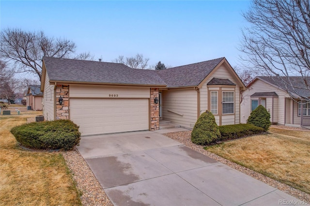 single story home featuring concrete driveway, stone siding, roof with shingles, an attached garage, and a front yard