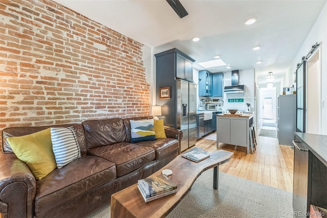 living room with brick wall, a barn door, light wood-style flooring, and a toaster