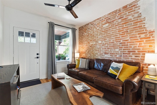 living room featuring ceiling fan, brick wall, and wood finished floors