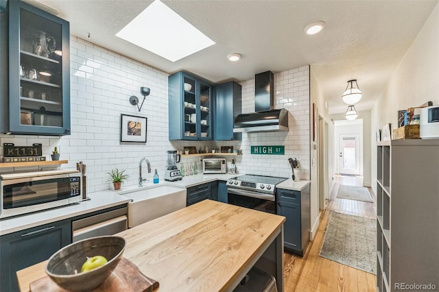 kitchen featuring wall chimney exhaust hood, electric range, a sink, and blue cabinets